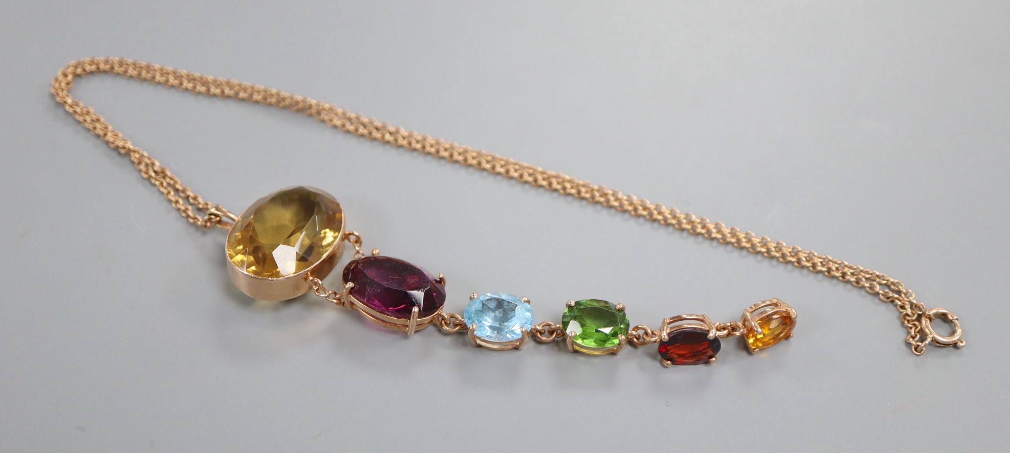 A yellow metal and graduated oval multi gem set pendant, on a yellow metal chain,